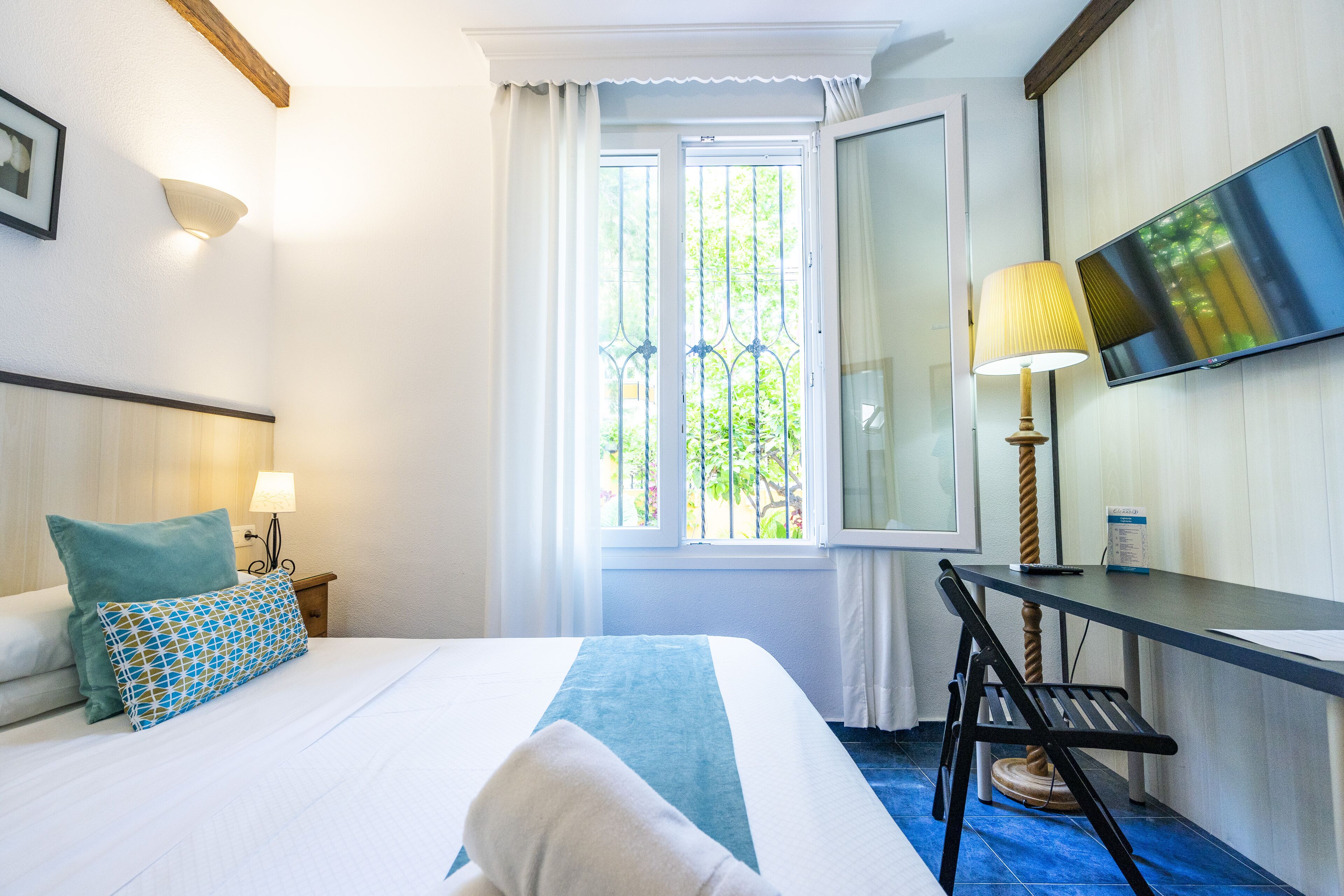 A hotel room with a bed, a desk, a chair, a TV, and a window with curtains.