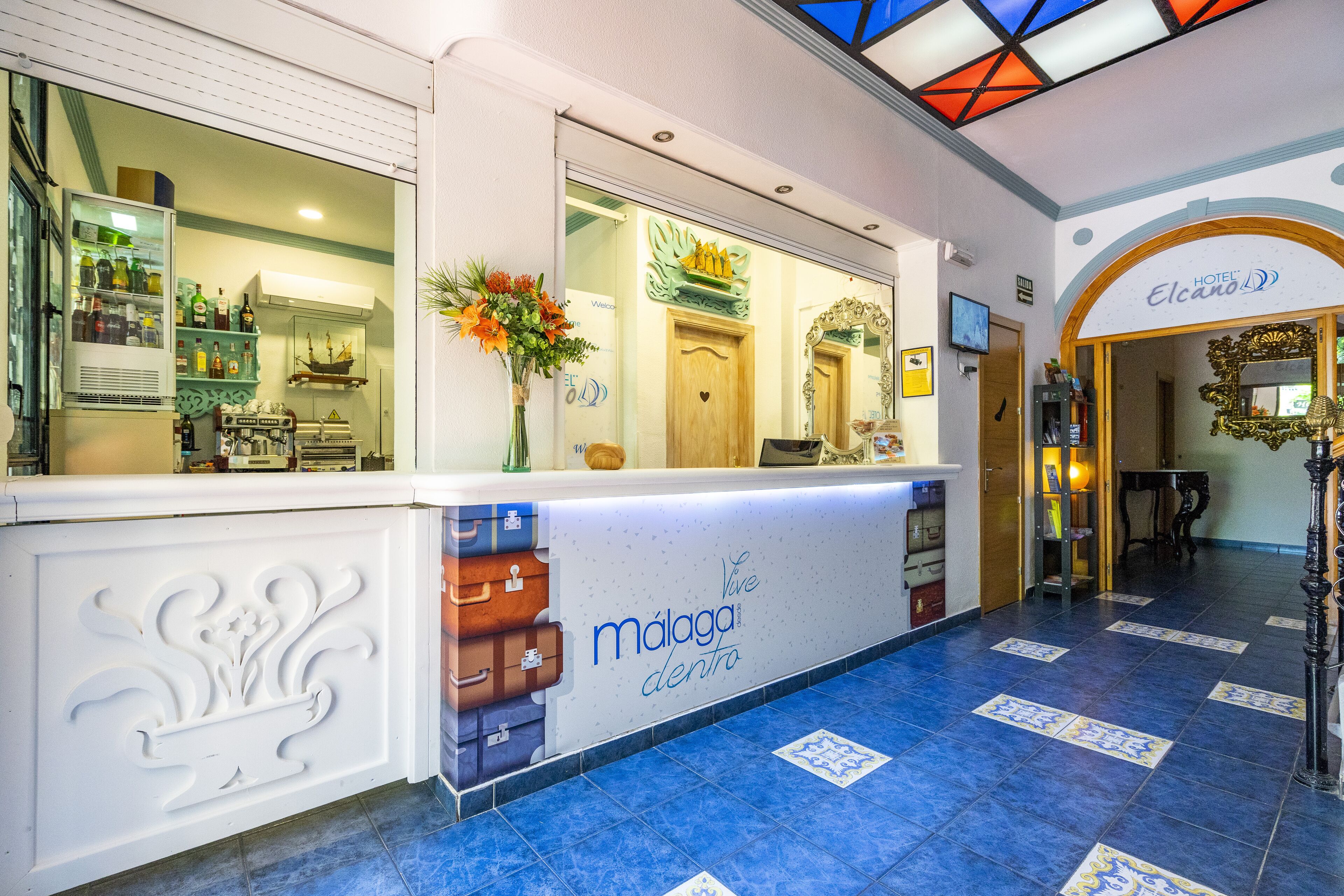 Zona de recepción con mostrador que muestra 'málaga dentro' y un cartel de 'Hotel Elcano'.