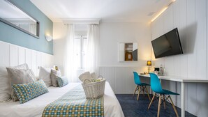 Habitación de hotel con cama, escritorio, dos sillas, televisión y ventana con cortinas.