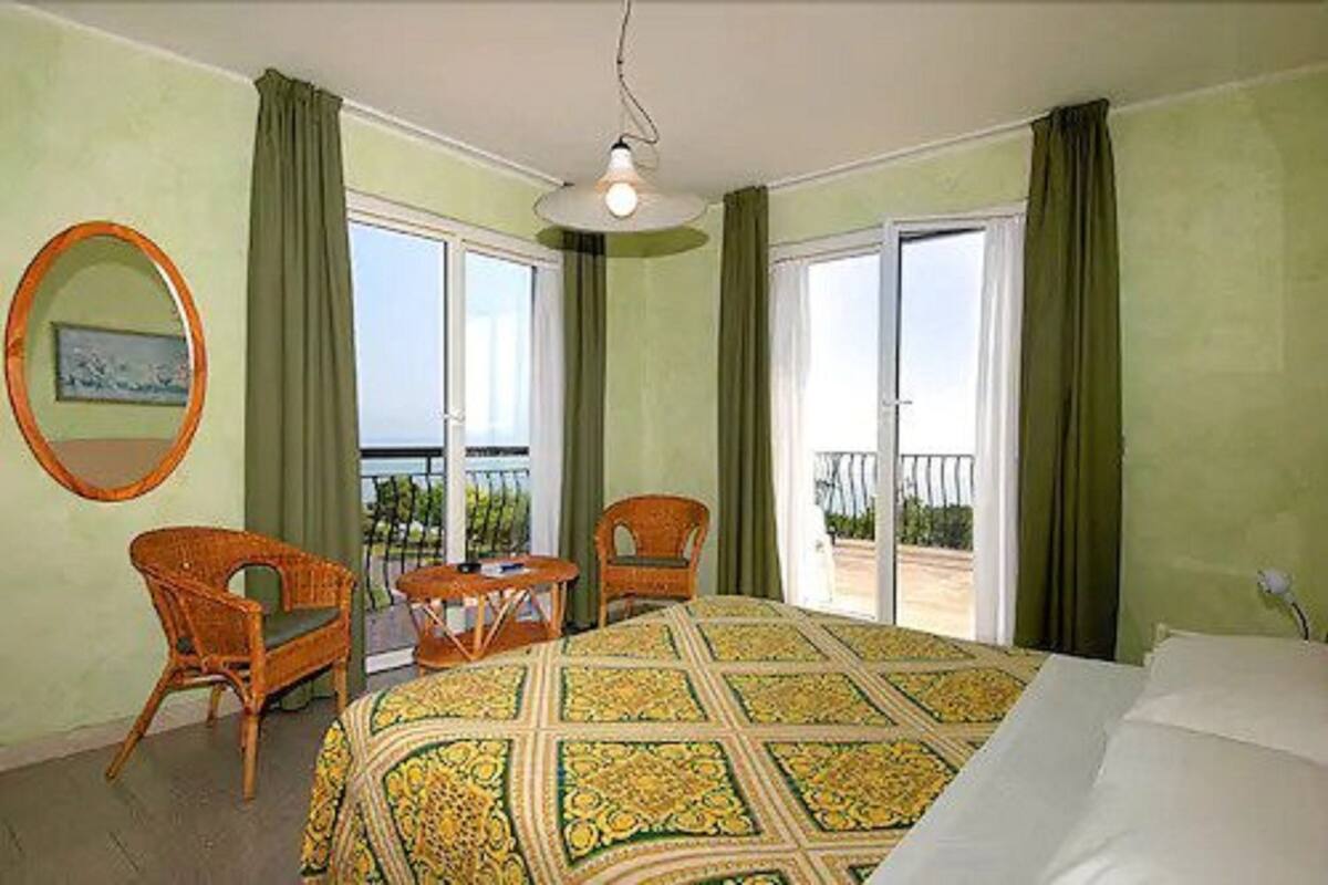 A hotel room with a bed, two chairs, a small table, and a balcony with a view.