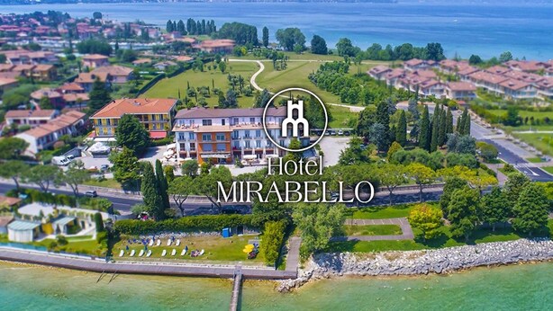 An aerial view of a coastal hotel with multiple buildings, a marina, and a clear view of the sea. - Mirabello (Sirmione)