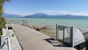 A wooden pier leading to a hotel named Mirabello, with a clear view of a calm lake and mountains in the background. - Mirabello (Sirmione)