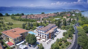 A residential area with a large building featuring a swimming pool, surrounded by greenery and a view of a lake. - Mirabello (Sirmione)