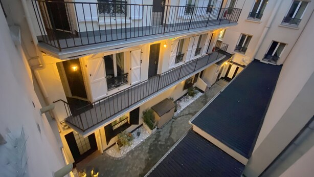 Un immeuble résidentiel à plusieurs étages, doté de balcons, d’une cour intérieure et d’une entrée sécurisée par un portail.