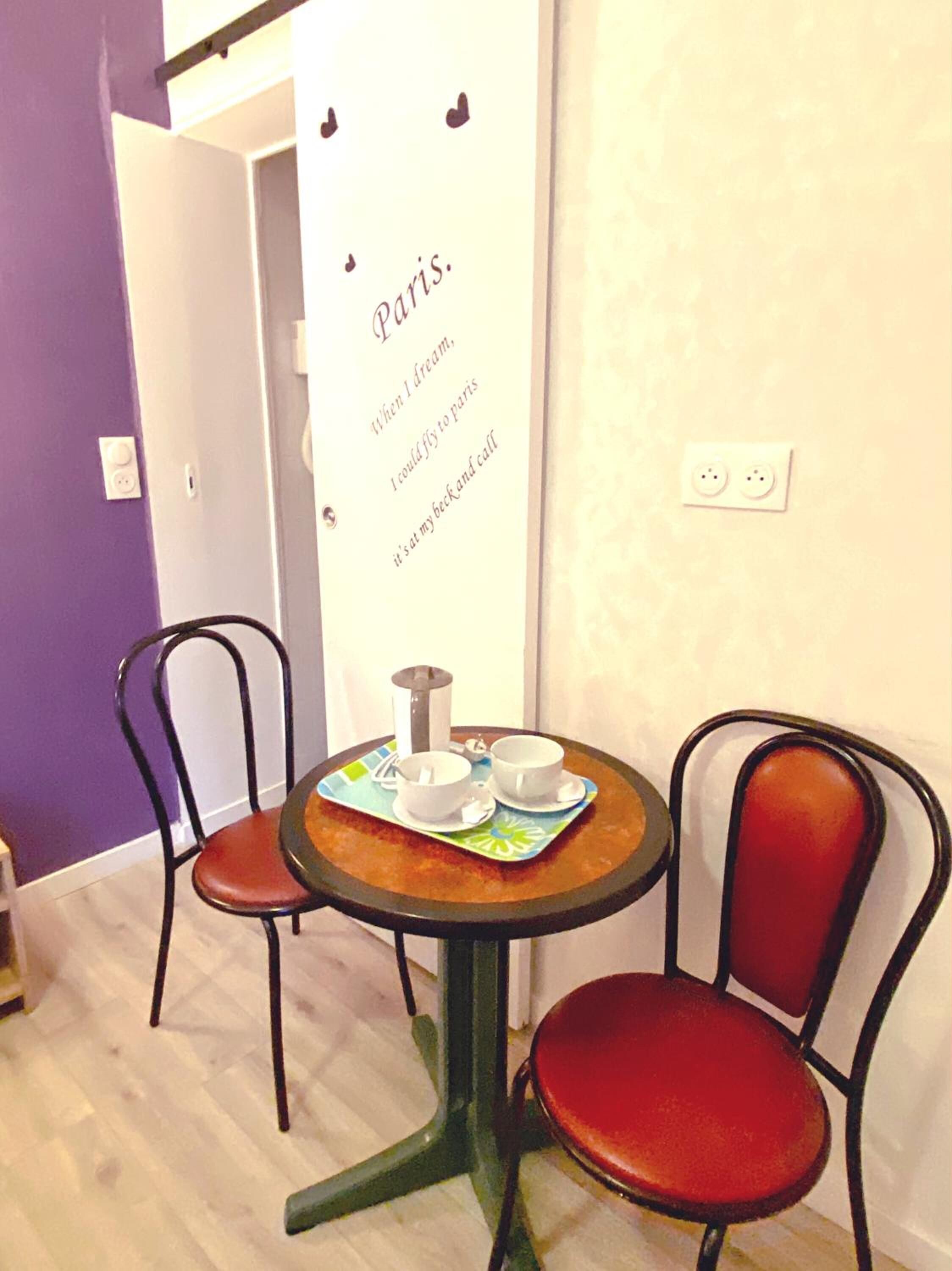 Ein kleiner runder Tisch mit zwei Stühlen, eine Tafel mit Text und eine Steckdose an der Wand.