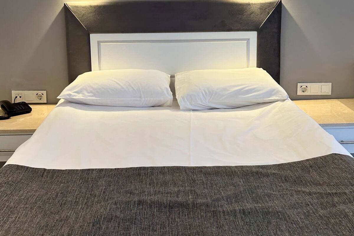 A neatly made bed with white linens and a gray throw blanket, flanked by two bedside tables with black lamps, and a modern headboard.