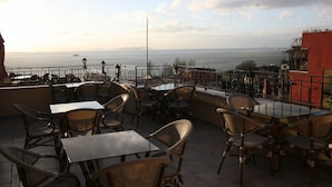 An outdoor seating area with tables and chairs, overlooking a body of water and distant land. - Hotel Peninsula (Istanbul)