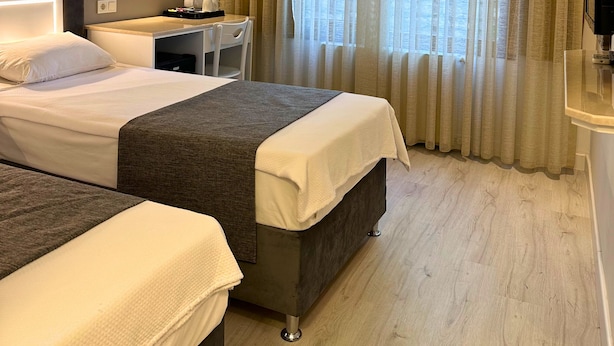 A hotel room with two beds, a desk, a chair, a large mirror, and a window with curtains. - Hotel Peninsula (Istanbul)