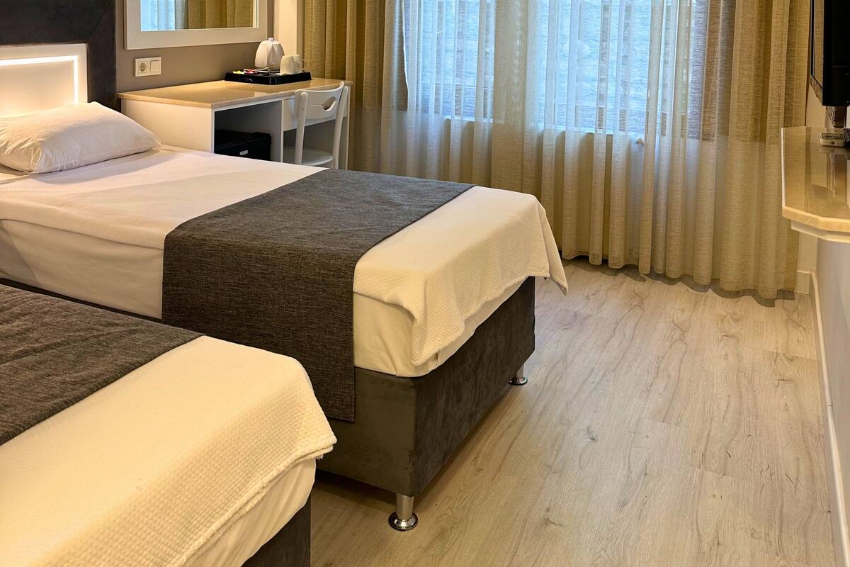 A hotel room with two beds, a desk, a chair, a large mirror, and a window with curtains.