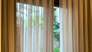 A room with a window covered by sheer curtains, a wooden table, and a view of greenery outside. - Hotel Peninsula (Istanbul)