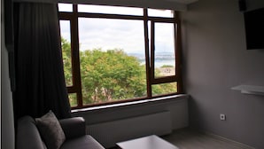 A room with a large window, a radiator, a grey sofa, and a white table. - Hotel Peninsula (Istanbul)