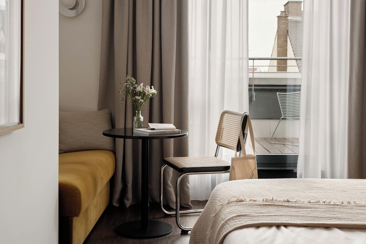 Una habitación de hotel con cama, una mesita con un jarrón de flores, una silla y un sofá.