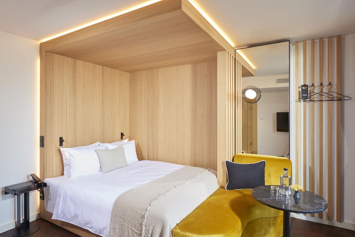 Una habitación de hotel con cama, mesita de noche, espejo y una pequeña mesa con silla.