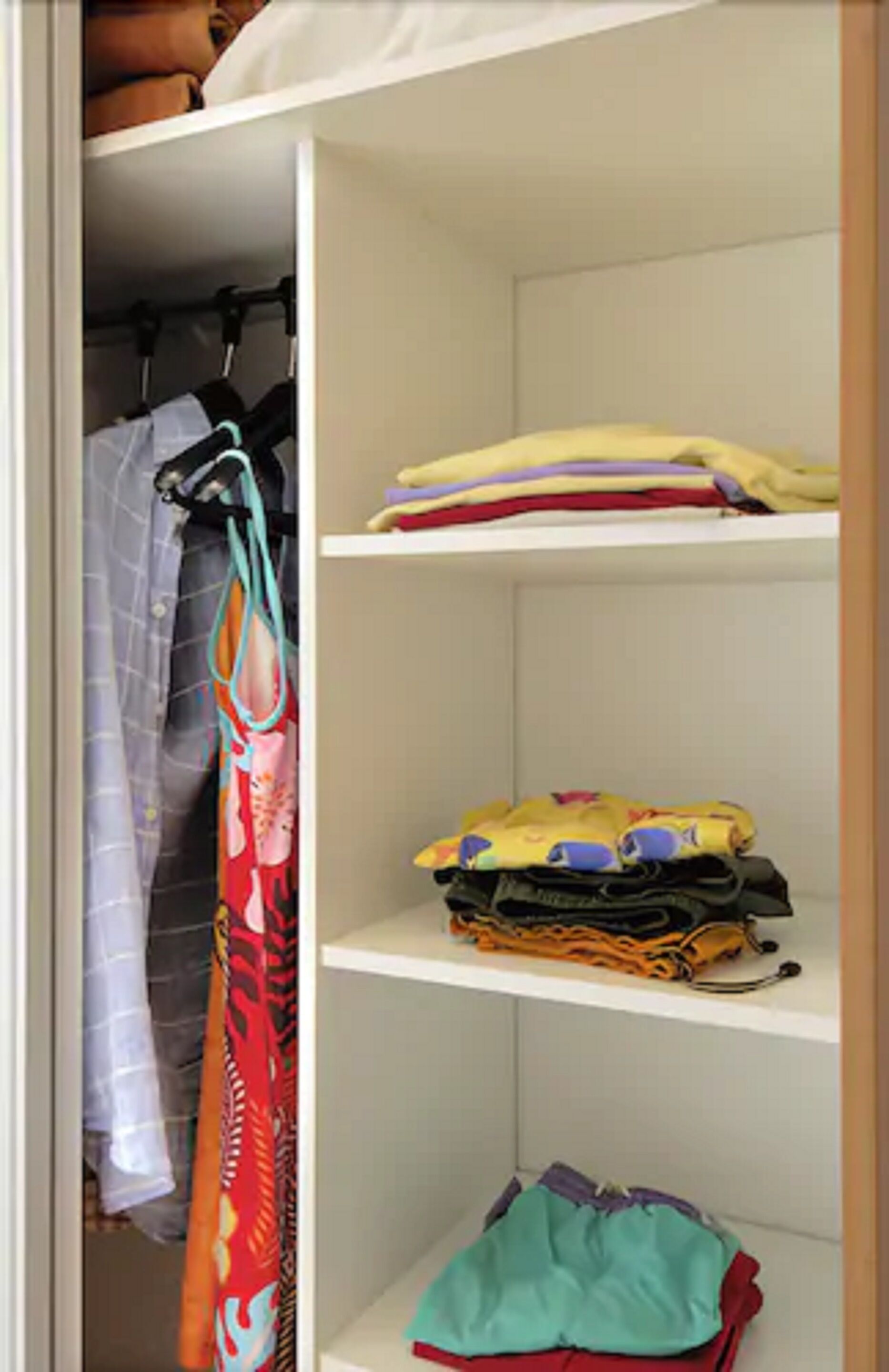 A closet with shelves holding folded clothes and a hanging rack with a colorful bag.