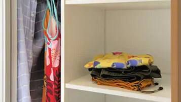 A closet with shelves holding folded clothes and a hanging rack with a colorful bag.
