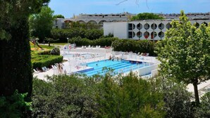 A swimming pool with multiple lanes, surrounded by trees and a building with arched windows in the background. - Residéal La Grande Motte (La Grande-Motte)