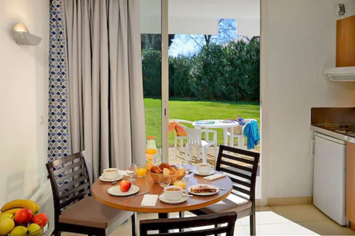 Ein Essbereich mit Tisch, gedeckt zum Frühstück, eine Küche und Blick auf einen Garten.