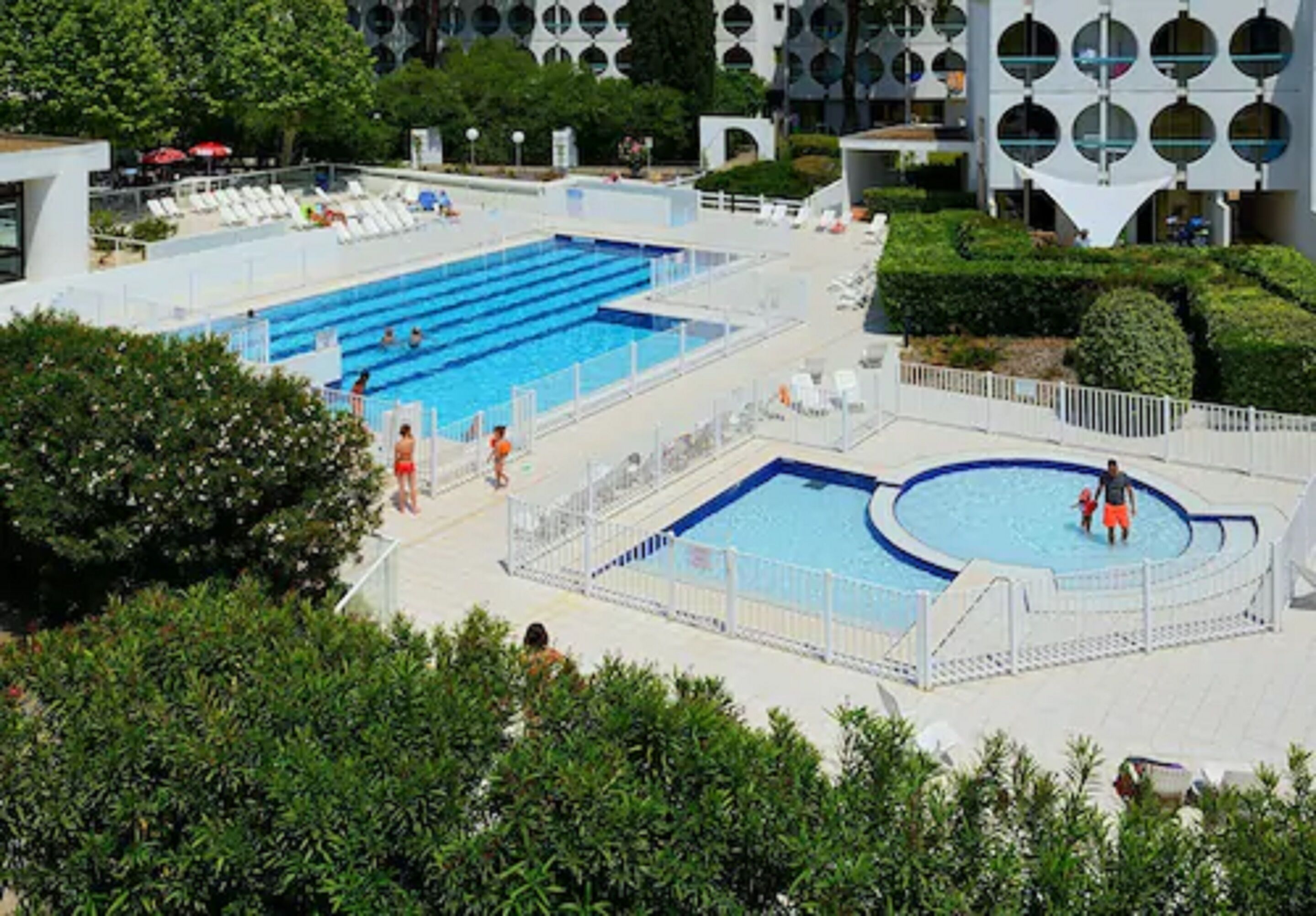 Une grande piscine extérieure avec plusieurs couloirs de nage, entourée de chaises longues et d’une clôture blanche.