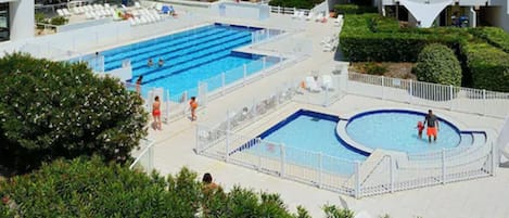 Une grande piscine extérieure avec plusieurs couloirs de nage, entourée de chaises longues et d’une clôture blanche.