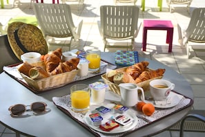 A breakfast setup with croissants, juice, and coffee on a table outdoors. - Residéal La Grande Motte (La Grande-Motte)