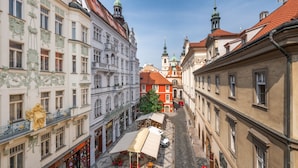 Eine gepflasterte Straße gesäumt von historischen Gebäuden, ein Café mit Außenterrasse und eine Kirche mit einer grünen Kuppel.