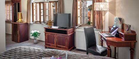 Quarto de hotel com uma cama, uma escrivaninha com um laptop, televisão e uma janela com cortinas.