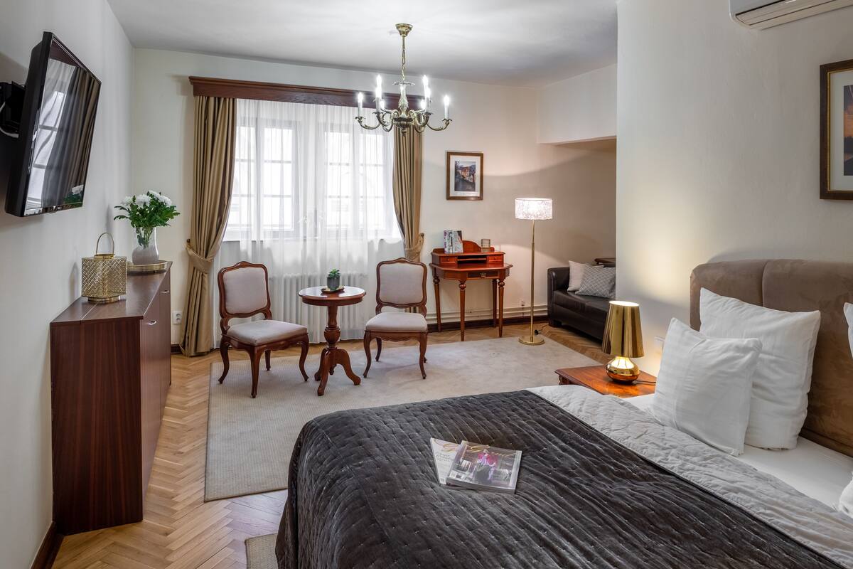Habitación de hotel con una cama grande, un escritorio, dos sillas, un televisor y una araña.