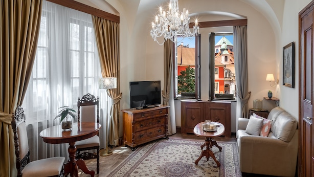 Ein gemütliches Wohnzimmer mit einer Chandelier, einem Fernseher, einer Couch und Blick auf ein Gebäude durch einen offenen Durchgang.