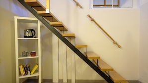 A staircase with wooden steps and black handrails, a white shelf with books and a kettle, and a window with wooden blinds. - Residenza Le Rondini (Florence)