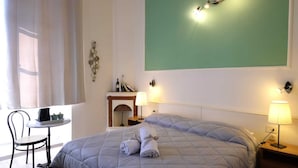 A hotel room with a bed, two bedside lamps, a small table with a chair, a fireplace, and a green wall. - Residenza Le Rondini (Florence)