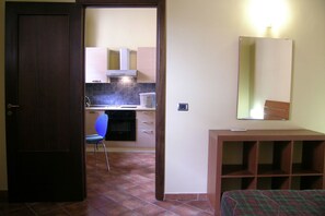 Une pièce comprenant un lit, un bureau, une chaise, un miroir et un coin cuisine avec une cuisinière et des placards.