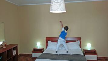 A child jumping on a bed in a hotel room with two bedside tables, a nightstand, and a lamp on each side.