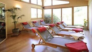 A sunroom with wooden ceiling beams, large windows, and multiple sun loungers with red cushions. - Partaneshof (Merano)