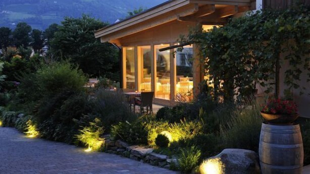 A modern, glass-enclosed outdoor dining area with a view of a mountain range. - Partaneshof (Merano)