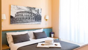 A hotel room with a bed, pillows, a nightstand, a lamp, a picture of the Colosseum, and a window with curtains. - Castelfidardo (Rome)
