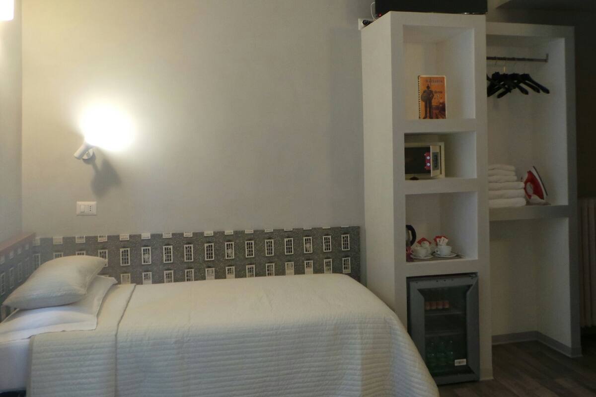 Ein Hotelzimmer mit einem Bett, einer Ablage mit Büchern und einer Mikrowelle sowie einem Heizkörper.