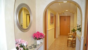 A hotel hallway with a reception desk, a mirror, a potted plant, and a door with a sign. - Castelfidardo (Rome)