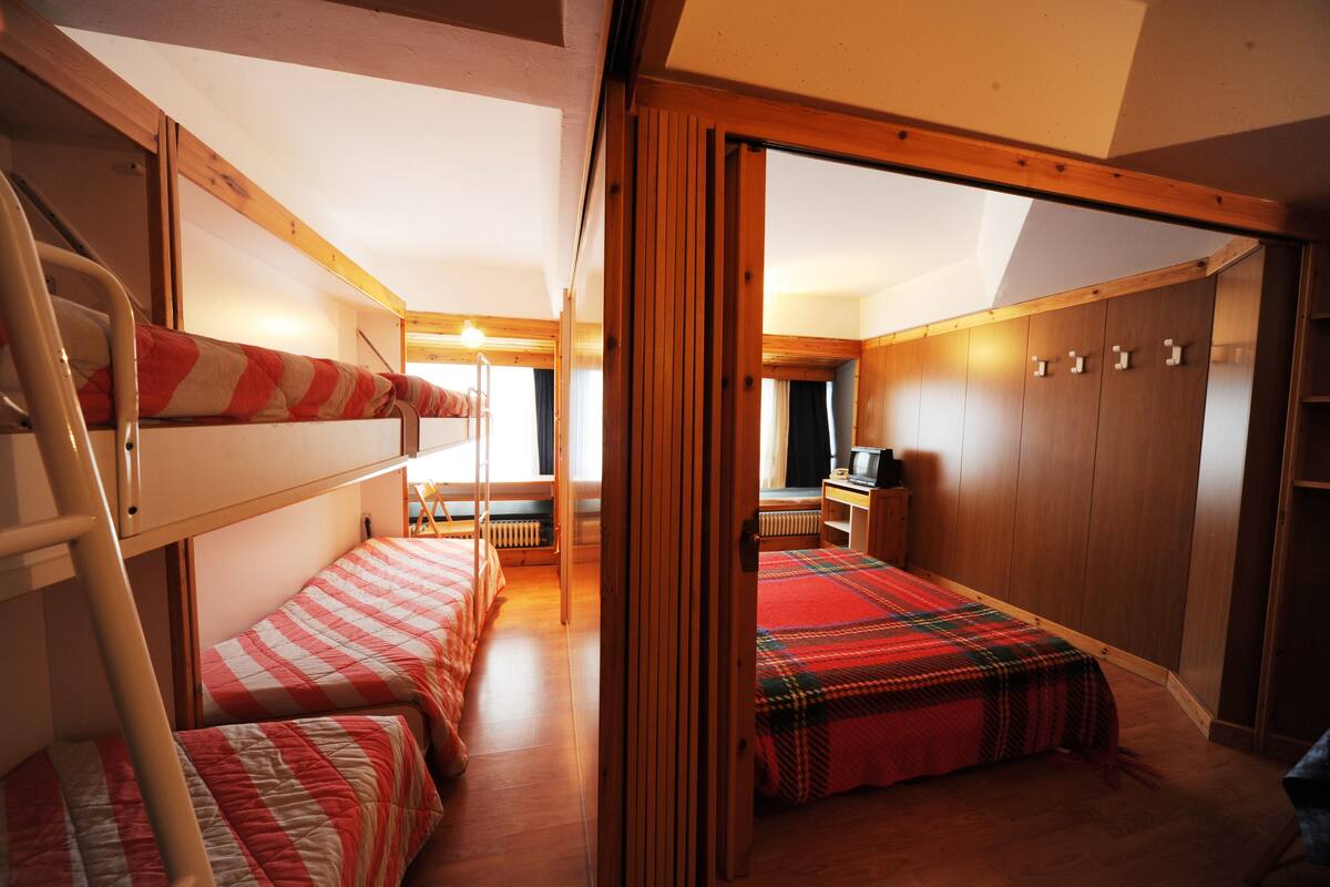 Un dormitorio compacto con literas, un armario de madera y una pequeña zona de escritorio.