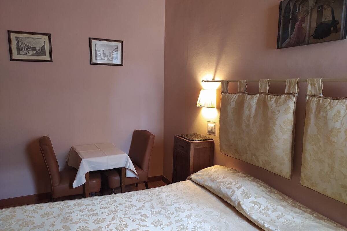 A hotel room with a bed, a table, two chairs, a nightstand, and a lamp.