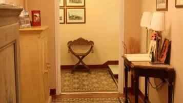 A hallway with patterned flooring, a wooden bench, a table with a lamp, and framed pictures on the wall.