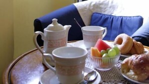 A breakfast tray with a teapot, cups, a bowl of fruit, and pastries on a table in a room with a view of a building through a window. - B&B A Florence View (Florence)