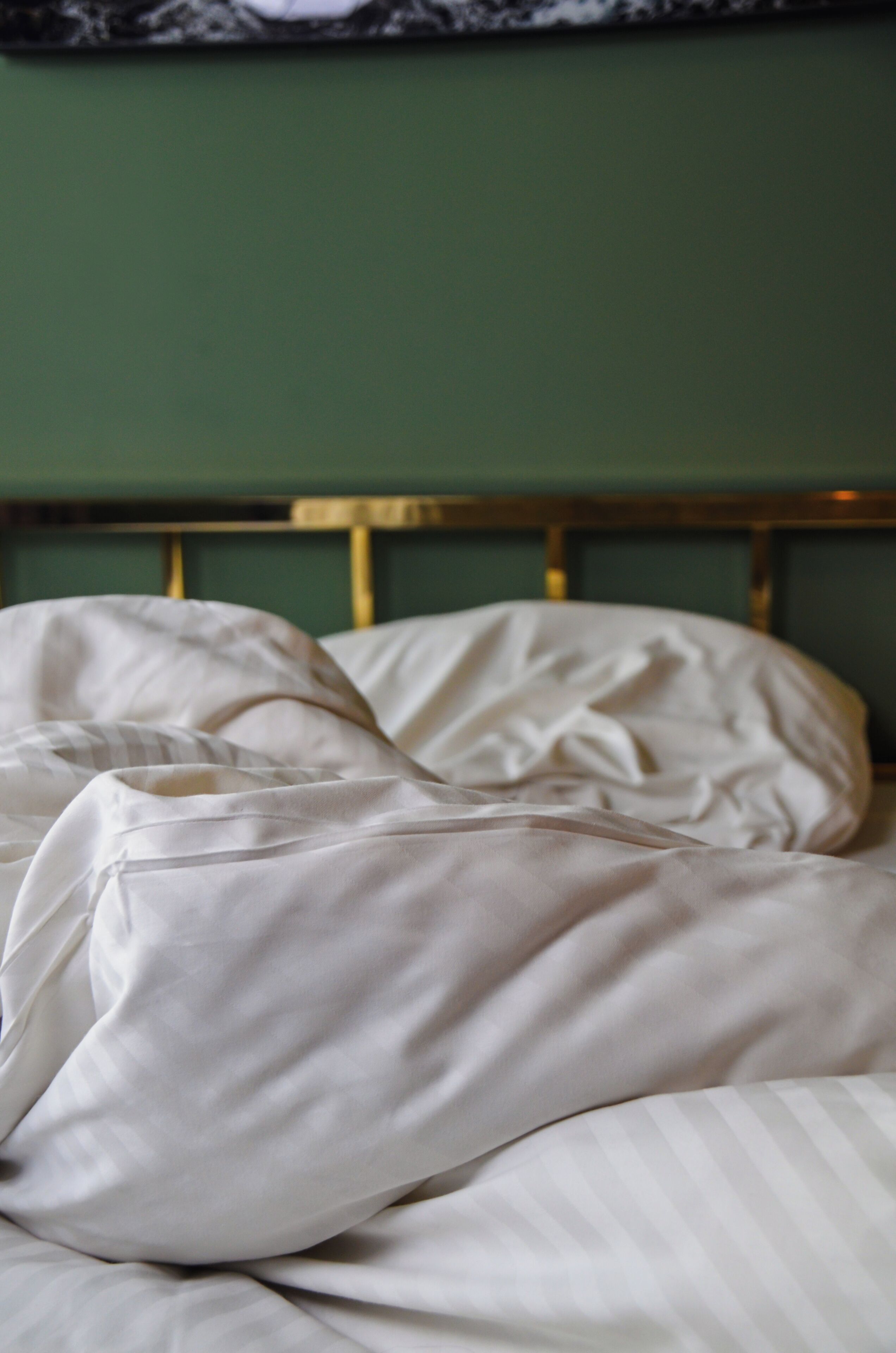 Un lit avec une literie blanche et un mur vert en arrière-plan.