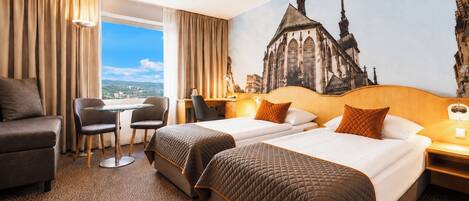 A hotel room with two beds, a desk, a chair, and a view of a cityscape.