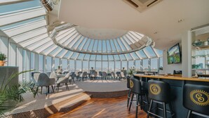 A modern interior with a high ceiling, a central seating area, and a bar with stools. - Cosmopolitan Bobycentrum – Czech Leading Hotels (Brno)