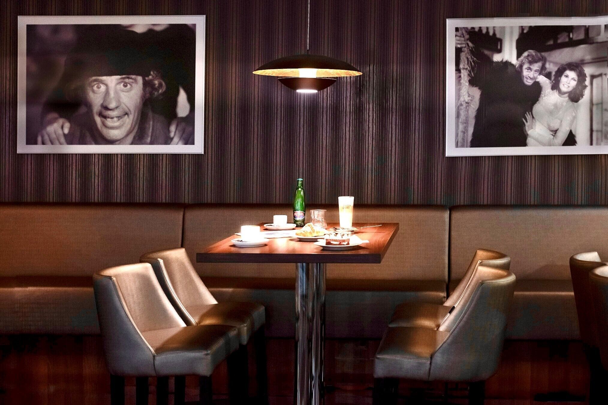Een restaurant met een zithoek met hokjes, een tafel met een fles, glazen en een kaars, en ingelijste foto's aan de muur.