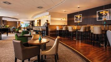 Un vestíbulo de hotel con mesas redondas, taburetes de bar y un piano.