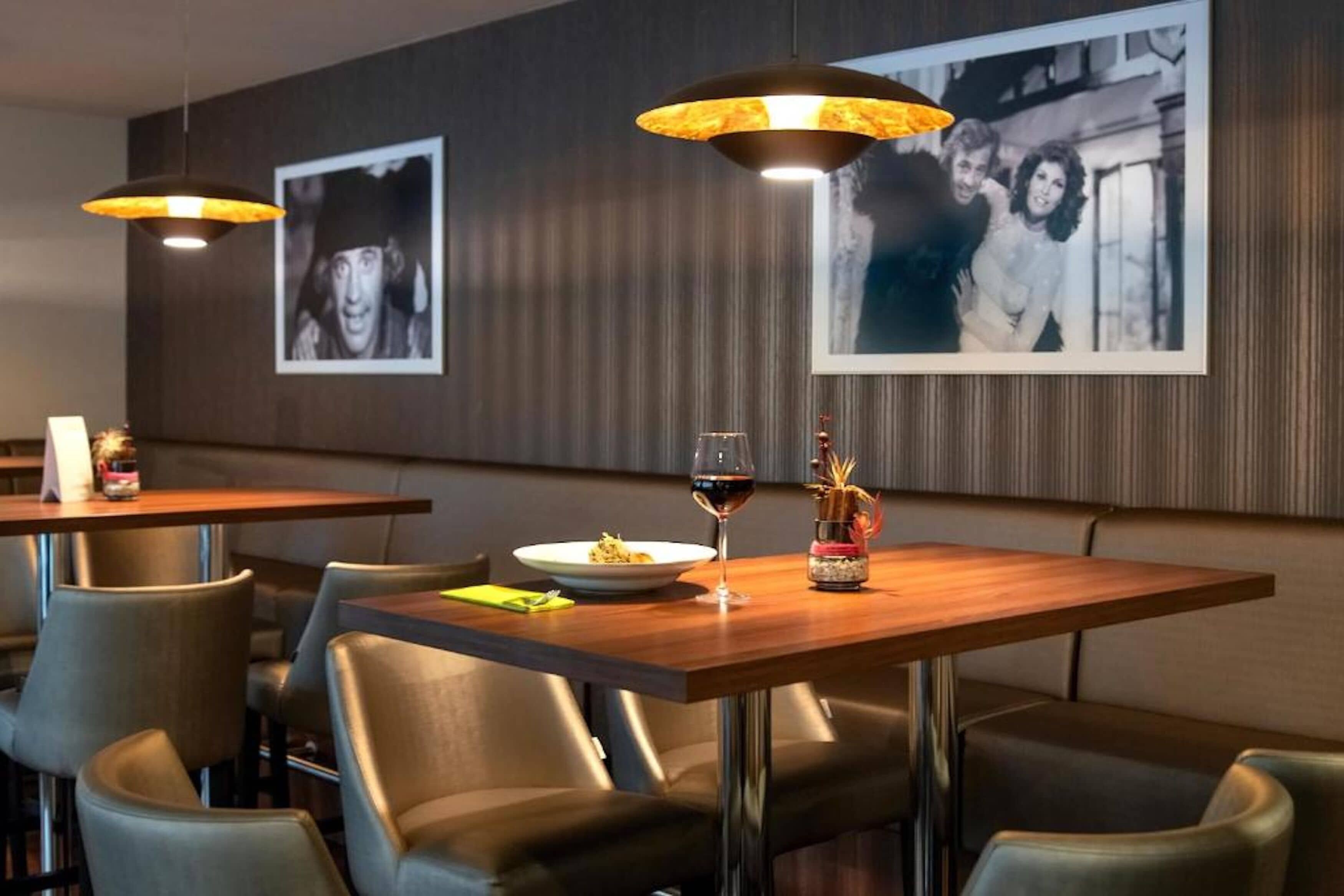 Un ristorante con tavoli e sedie in legno, fotografie incorniciate alle pareti e un bicchiere da vino su un tavolo.