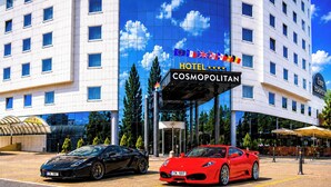 A hotel with a modern facade, a prominent sign reading 'HOTEL COSMOPOLITAN,' and two luxury sports cars parked in front. - Cosmopolitan Bobycentrum – Czech Leading Hotels (Brno)