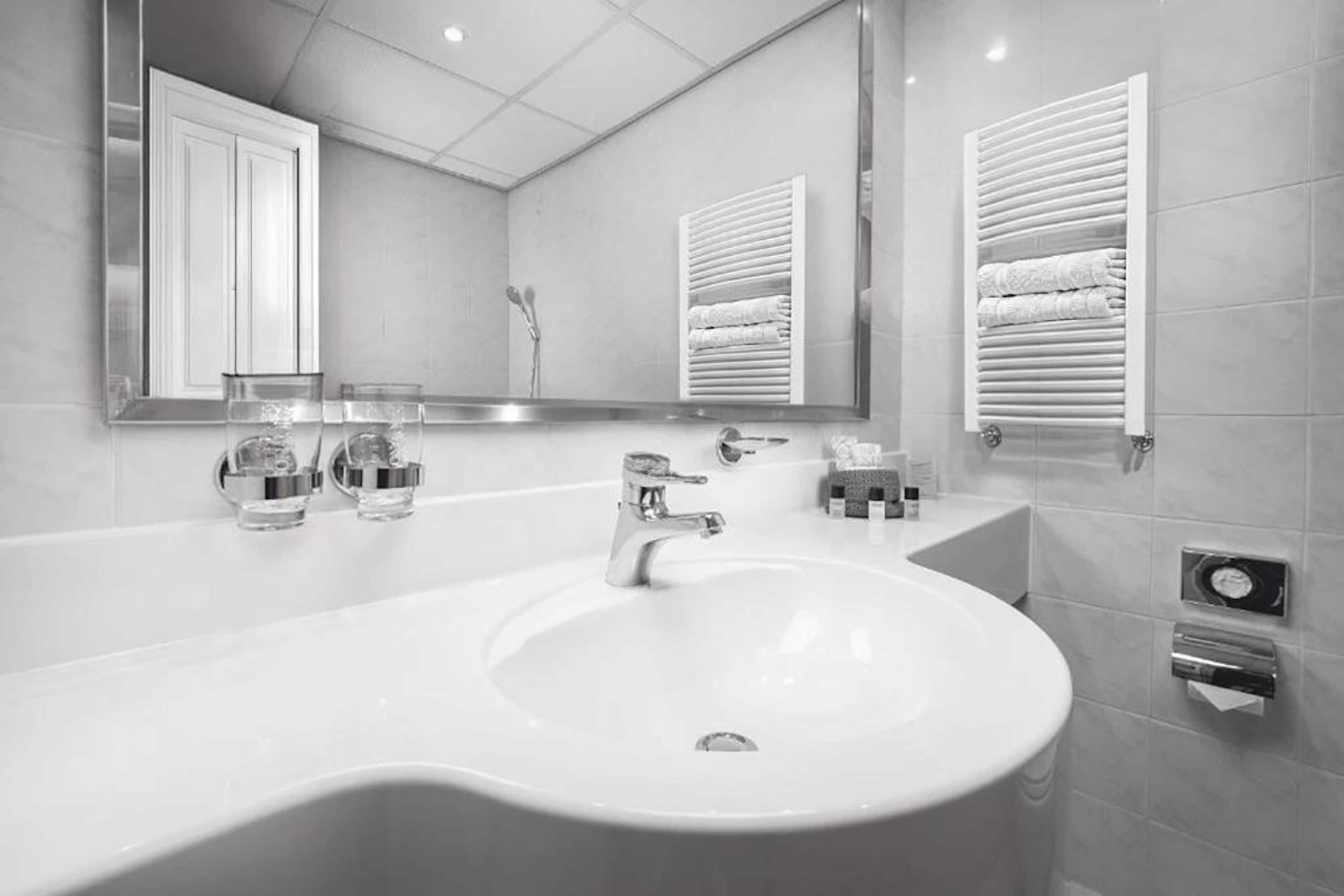 A modern bathroom with a large sink, two faucets, a mirror, and towel racks.