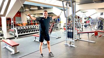 Een fitnessruimte met diverse trainingsapparaten, waaronder gewichten en banken.